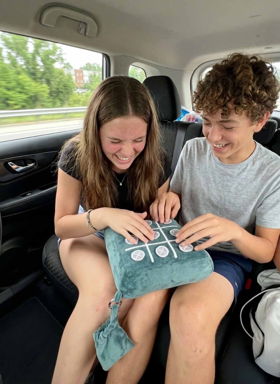 Two teenagers laughing while playing tic-tac-toe on the pillow in a car