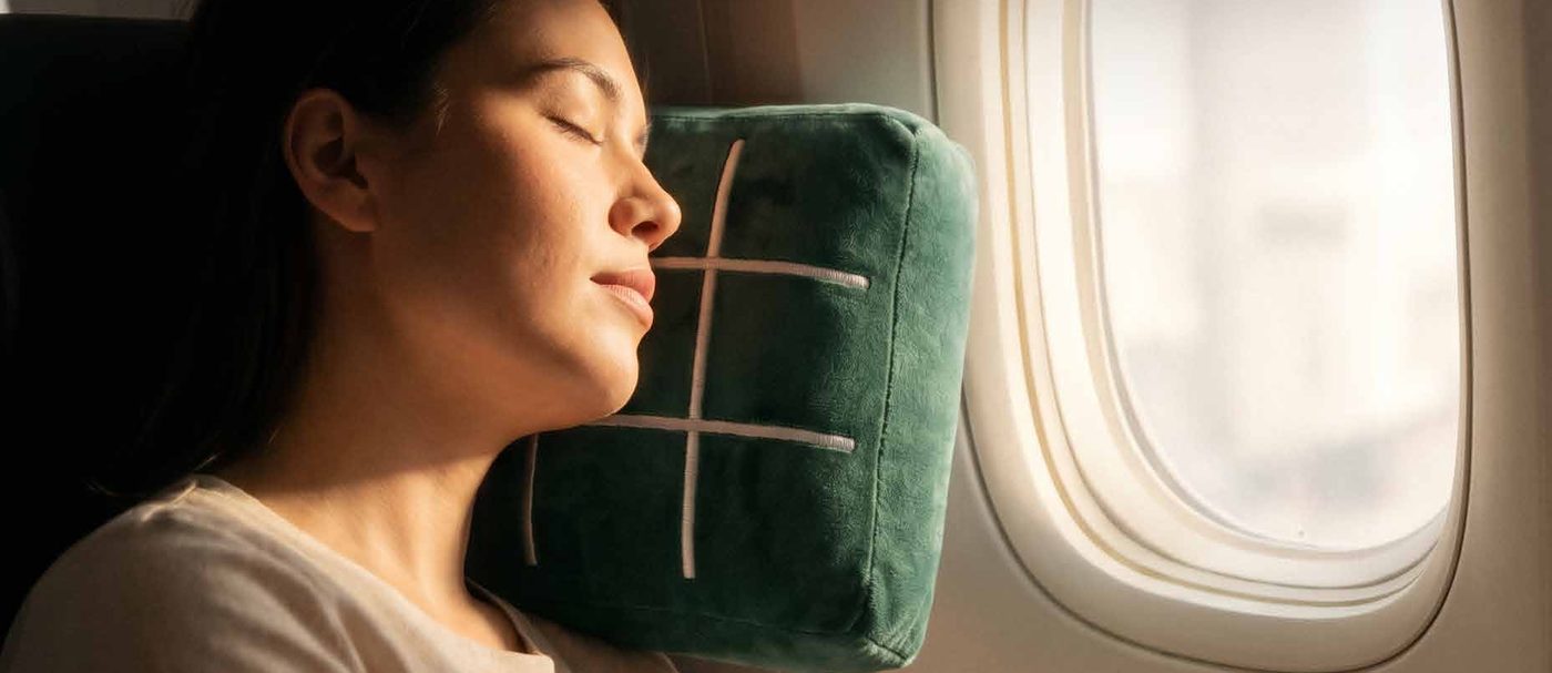 Traveler asleep against the Forest Green TicTac2Go pillow by a plane window